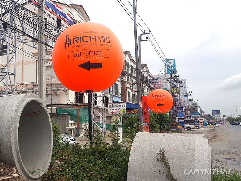 บอลลูนโฆษณาสีส้มตั้งพื้น บอกทาง Sale Office โครงการ The Rich Ville ริมถนน
