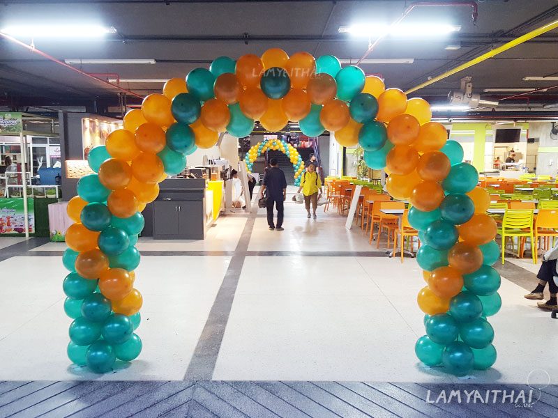 ซุ้มลูกโป่งโค้งสีเขียวส้มตกแต่งทางเข้าศูนย์อาหารในห้างสรรพสินค้า