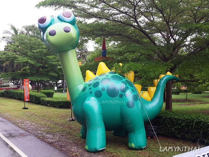 บอลลูนโฆษณารูปไดโนเสาร์สีเขียวขนาดใหญ่ตั้งกลางสวนงานอีเวนต์กลางแจ้ง