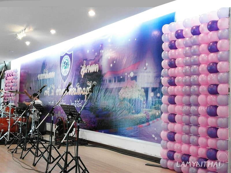 ผนังลูกโป่งสีชมพูม่วงตกแต่งข้างเวทีงานเลี้ยงในหอประชุม