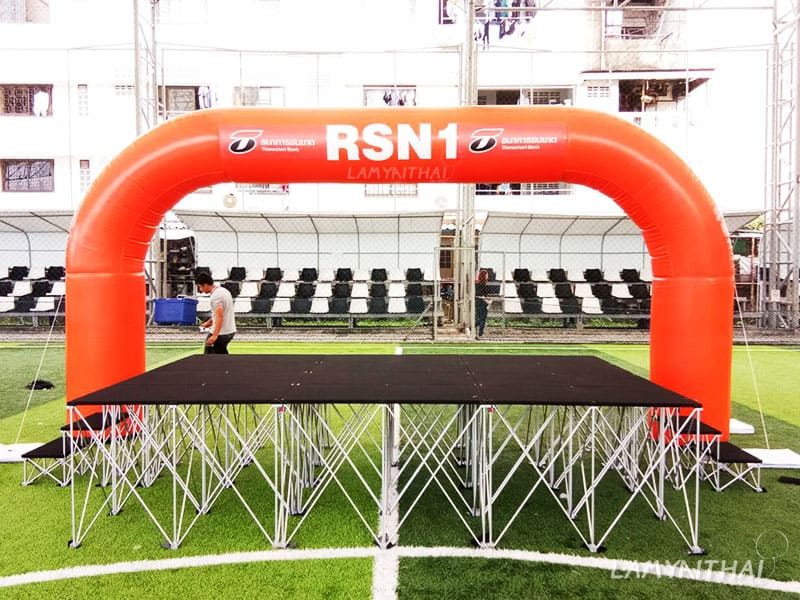 ซุ้มพองลมสีส้ม RSN1 คร่อมเวทีในสนามฟุตบอลหญ้าเทียม