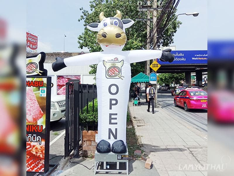 ตุ๊กตาโบกรูปวัวสีขาวมีป้าย OPEN หน้าร้านอาหารริมถนน